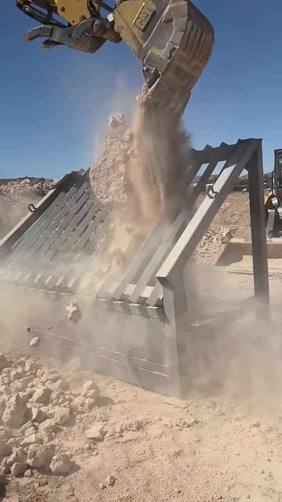 Full grizzly screen loaded with rock, dust in the air
